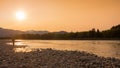 A fisherman walking along a gravel bar beside the Skeena River at sunset