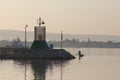 The fisherman will paddle on a small boat in the rays of the rising sun floating past the lighthouse located at the entrance to th