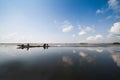 Fisherman in wooden boat crusing in the lake with reflection with cloudy blue sky background