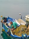 Fisherman working on his fishing nets in traditional weathered blue wooden boat in the port of Kavala