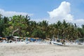 Fishermen carry a boat on a virgin beach in Bali. Fishing boats on white sand. Coconut trees and blue sky with clouds on Royalty Free Stock Photo