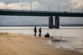 Fishermen on the sandy river bank near the bridge Royalty Free Stock Photo