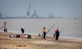 Fishermen fishing off the beach with cranes in Yarmouth Harbour in the back ground, near Lowestoft, Norfolk, UK Royalty Free Stock Photo