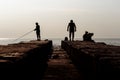 Fishermen fishing on the pier. Humans interaction on the breakwater. Silhouette photo.
