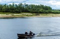 Fishermen move in a motorboat through the water against a background of green trees and a blue sky