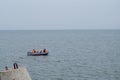 Fishermen with rods dressed in protective vests sitting with backs to viewer in black rubber boat on background of sea horizon Royalty Free Stock Photo