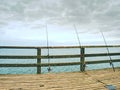 Fishers rods against handrail of wooden bridge. Fishing on harbor mole. Overcast day