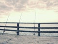 Fishers rods against handrail of wooden bridge. Fishing on harbor mole. Overcast day