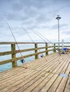 Fishers rods against handrail of wooden bridge. Fishing on harbor mole. Overcast day