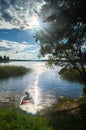 Fishers` simple motorboat, moored to the riparian forest of the lake Seliger under the radiant blinding sunlight, Russia.