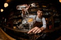 Fisheye shot male bartender pouring a cocktail from the measuring cup to the glass with orange zest