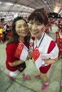 Fisheye shot of two female with SG50 tattoo on faces, hold mini national flags with pride and joy