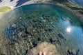 Fisheye view from above of alpine transparent lake and human feet into the water, in idyllic uncontaminated environment once cover Royalty Free Stock Photo
