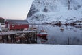 Fishing boat anchored on pier with red village in winter at Lofoten Royalty Free Stock Photo