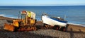 Fishing boat being pulled out of the sea by rusty bulldozer tractor on weybournes norfolk beach