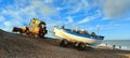 Fishing boat being pulled out of the sea by rusty bulldozer tractor on weybournes norfolk beach