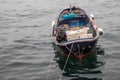 Fishing boat with deep blue accent surrounded by buoy and net inside. Anchored on water next to shore with ropes.