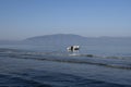 A fishing boat floating in blue sea water, anchored by a rope from the beach with white waves and pebbles Royalty Free Stock Photo