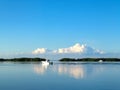 Fishing boat out on the water in Florida Keys with land in the distance and huge fluffy clouds reflected in the very blue ocean - Royalty Free Stock Photo