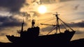 A fishing boat on the sea as silhoutte at sunrise looks like a pirate ship. Photographed from below at the water level. Radio ante