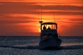 A fishing boat, silhouetted by the setting summer sun and a brilliant orange sky, makes its way to harbor.