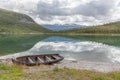 Fishing boat on a still lake in Norway and high mountains in background. Norwegian landscape with a boat on lake against mountains Royalty Free Stock Photo