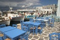 Taverna tables and chairs on a terrace with fishing boats in the background, at Naoussa, Paros, Greece. Royalty Free Stock Photo