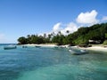 Fishing boats in blue water next to sandy beach with coconut palms and blue sky with white clouds