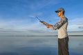 Fishing casting. Fisherman do cast by baitcasting spinning rod at lake on blue sky background