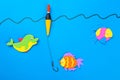 Fishing concept. Colorful toy fish with a hook and fishing buoy on blue background.