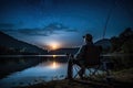 Fishing Man is Sitting at Night by Lake, Fishing Chair, Outdoor Tent, Fisherman Holds a Fishing Rod Royalty Free Stock Photo