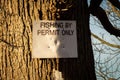 Fishing by permit only sign attached to a large tree in the winter sun Royalty Free Stock Photo