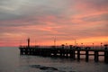 Fishing pier on the ocean with a colorful and golden sunset. Ocean beach sunrise and dramatic colorful sky clouds. Royalty Free Stock Photo