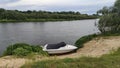 Fishing on the river in summer. A plastic motorboat covered with an awning is moored to the sandy shore. On the banks grow bushes Royalty Free Stock Photo