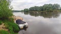 Fishing on the river in summer. A plastic motorboat covered with an awning is moored to the sandy shore where feeder rods are set Royalty Free Stock Photo