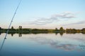 fishing rod against bright lake with reeds forest and bridge at sunny summer day