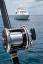 Fishing rod on a boat over blue sky and white sailing boat in the sea