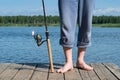 Fishing rod and legs of the fisherman stand on the pier, background close-up Royalty Free Stock Photo