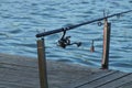 Fishing rod with a reel on the gray wooden planks of the bridge near the blue water Royalty Free Stock Photo