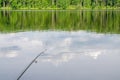 Fishing rod, water surface, float, day, reflection of clouds. Royalty Free Stock Photo