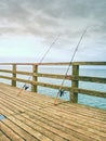 Fishing on sea bridge. Fishers rods against the wooden handrail of the beach mole.