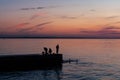 Fishing on sea, colorful morning sunrise, people on pier fish, red-orange sunrise, smooth water surface.