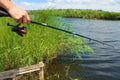 Close-up of a fishing rod with a reel in male hands against the backdrop of a channel in the wild.