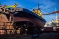 Fishing vessel maintenance in shipyard drydock. Workers repair, repaint hull, propeller, docked boat under clear sky Royalty Free Stock Photo