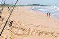 Fishingrods are stuck in the sand, footprints in several directions, a man is pulling his fishing rod, to couples walk