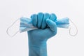 Fist Hand in medical blue latex protective glove holding a medical mask on white background Royalty Free Stock Photo