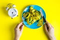 fist on a plate with a measuring tape. Alarm clock. Woman hands hold fork and knife