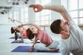 Fit adult women and man practicing yoga poses in fitness class. Group of healthy strong people doing fit exercises in white gym