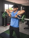 A fit asian guy does upright rows with an EZ curl bar at an open air gym. Traps upper back and shoulder exercise