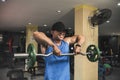 A fit asian guy does upright rows with an EZ curl bar at an open air gym. Traps upper back and shoulder exercise